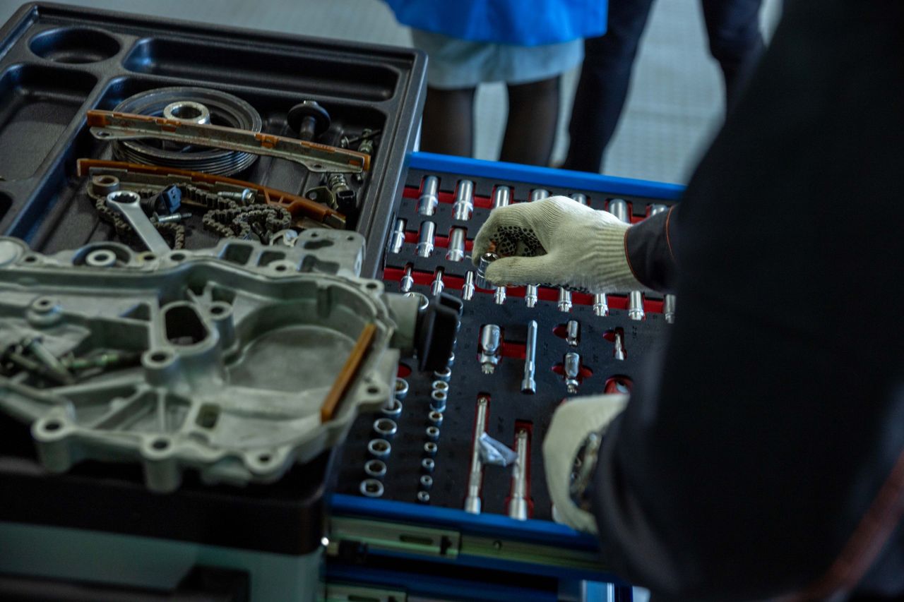 A mechanic in gloves organizing engine parts and tools in a workshop setting.